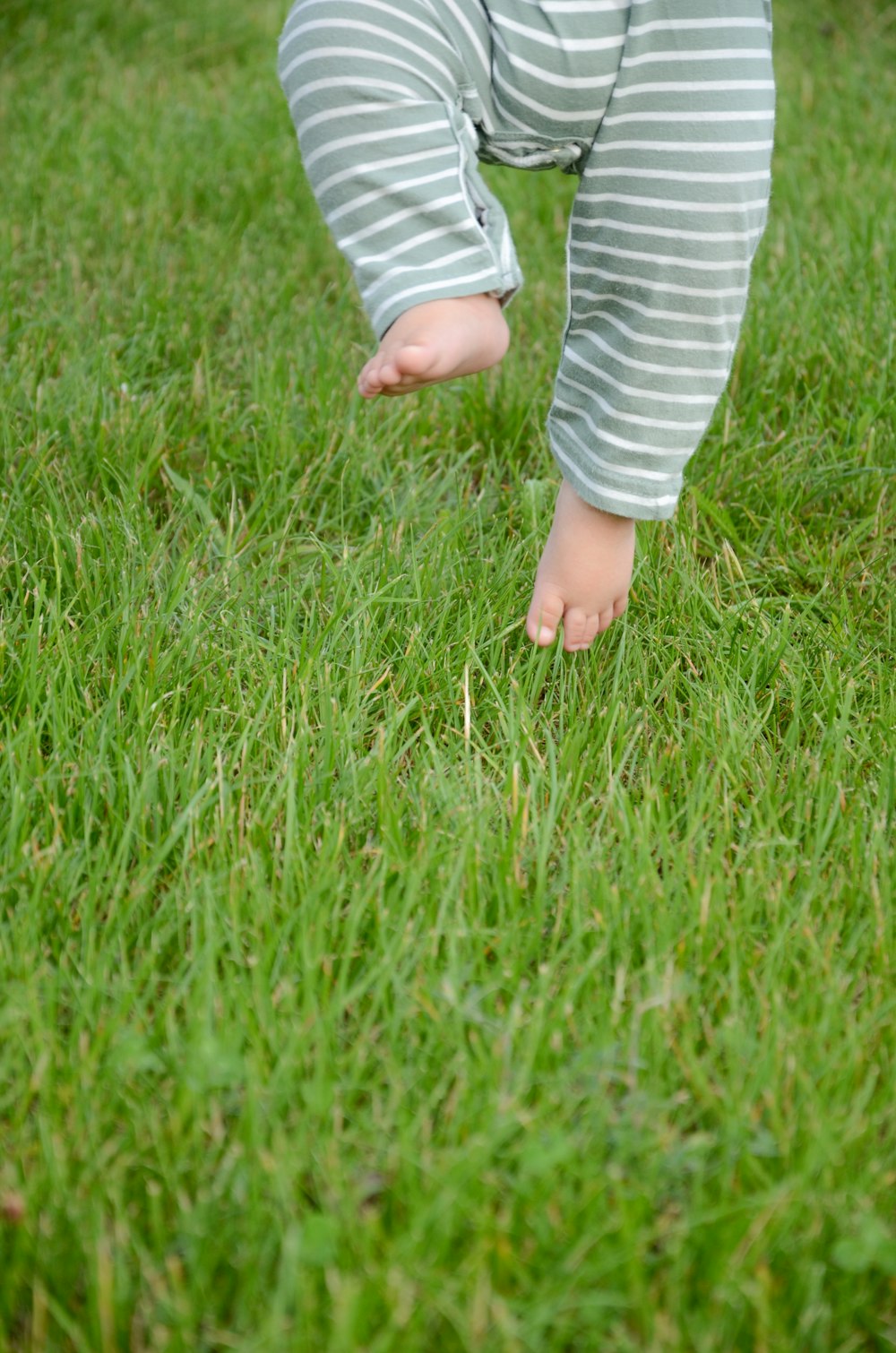 child in white and blue striped long sleeve shirt standing on green grass field during daytime