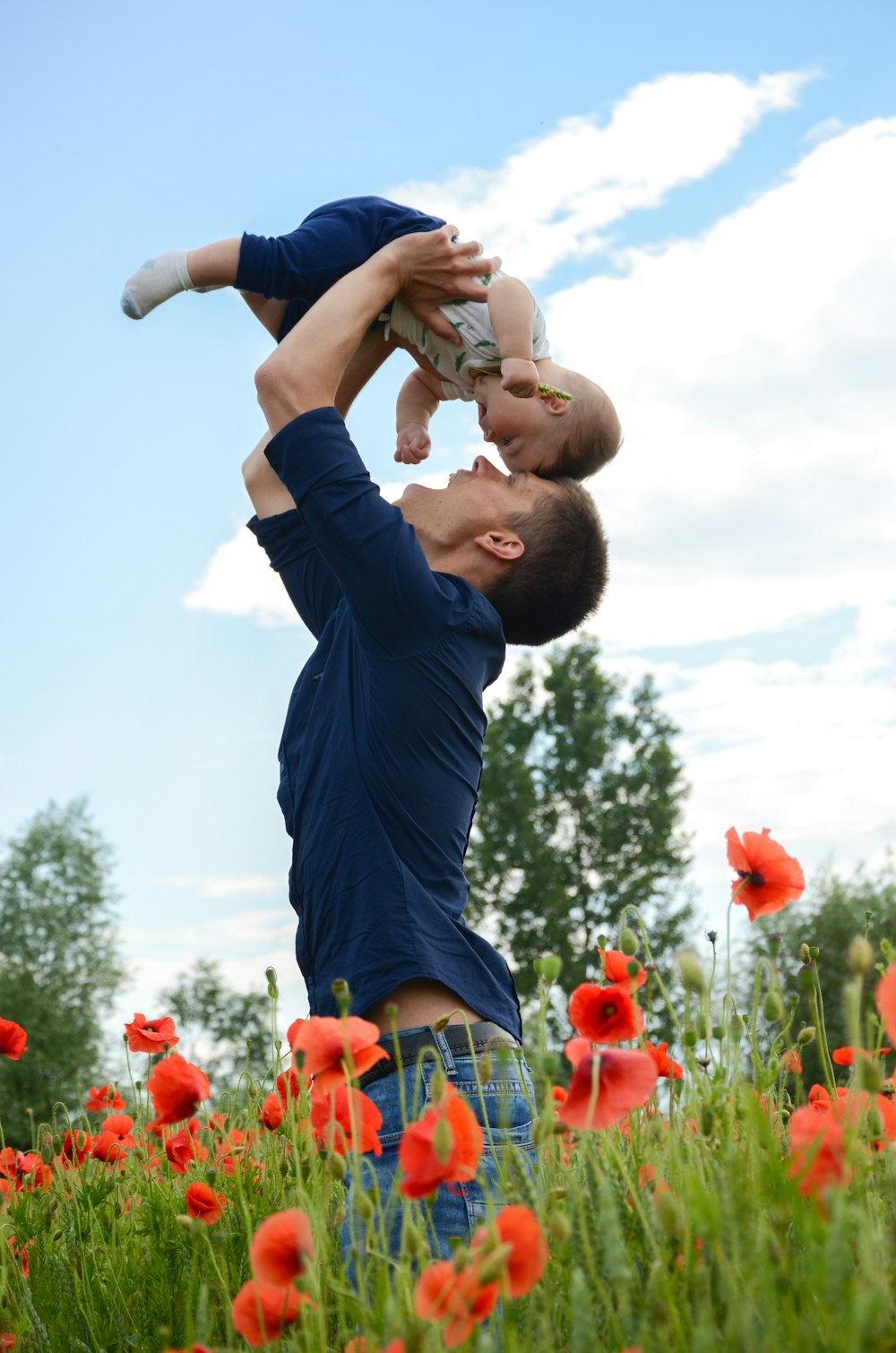 man in blue long sleeve shirt carrying baby in white onesie