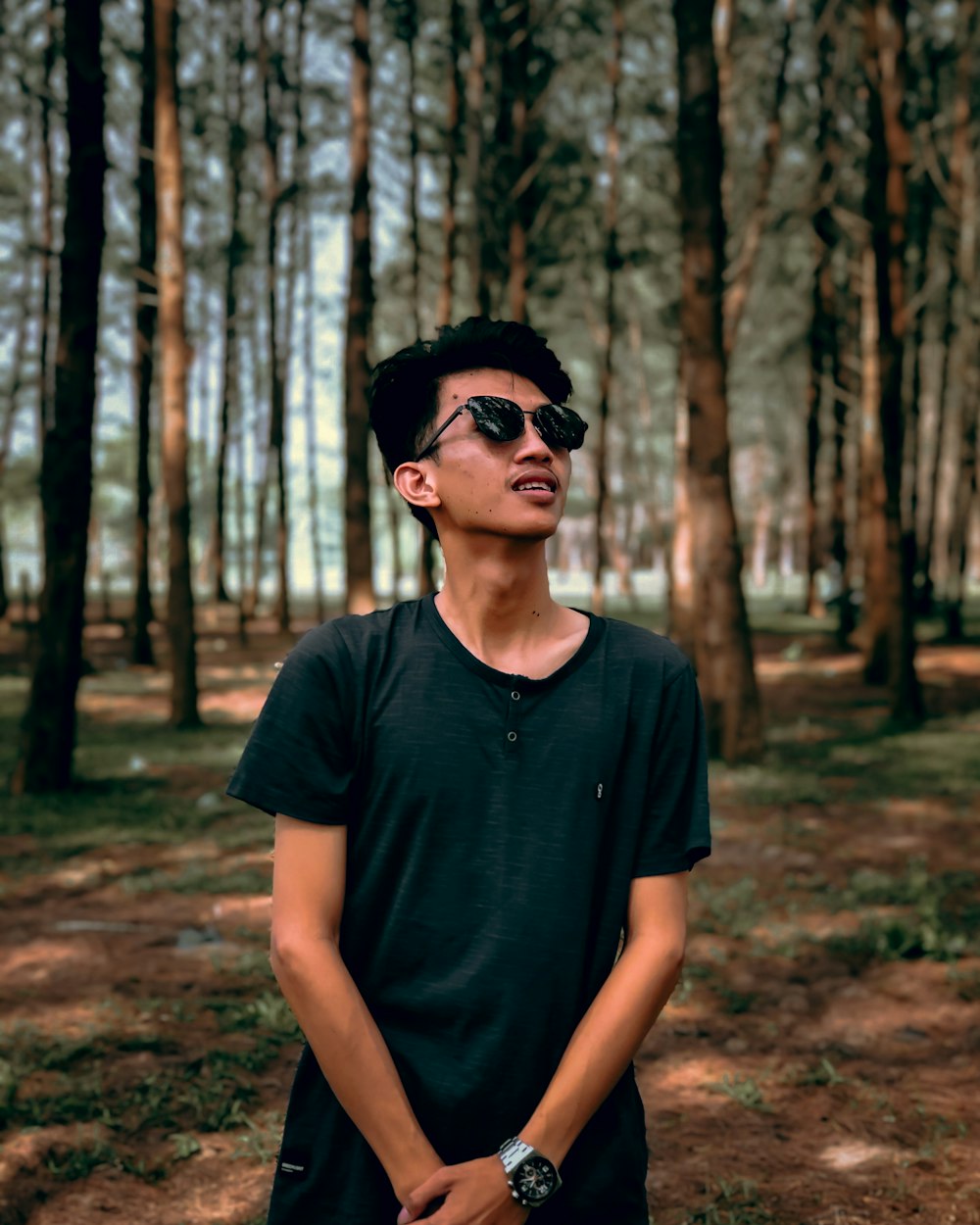 man in black crew neck t-shirt wearing black sunglasses standing in forest during daytime