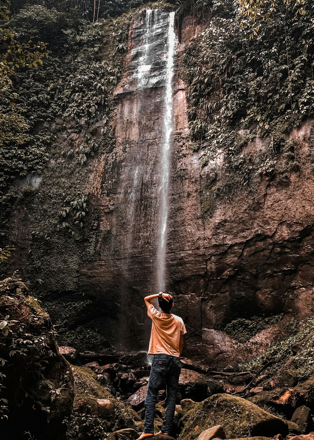 woman in brown hoodie standing in front of waterfalls during daytime