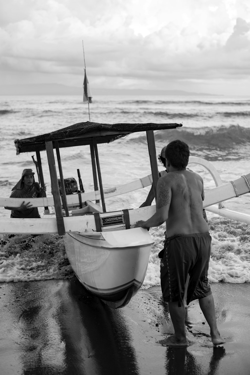 topless man in black shorts standing beside white boat on beach during daytime