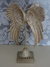 A decorative object resembling golden wings attached to a vertical stand, set against a patterned dark gray and white background.