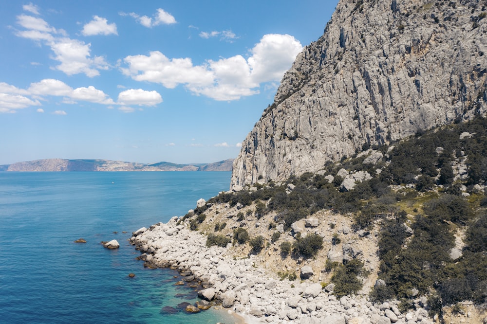 gray rocky mountain beside blue sea under blue sky during daytime