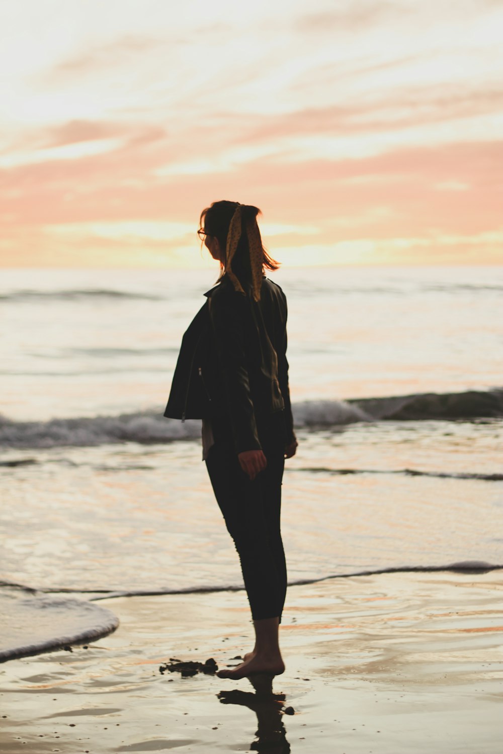 woman in black coat standing on beach during sunset