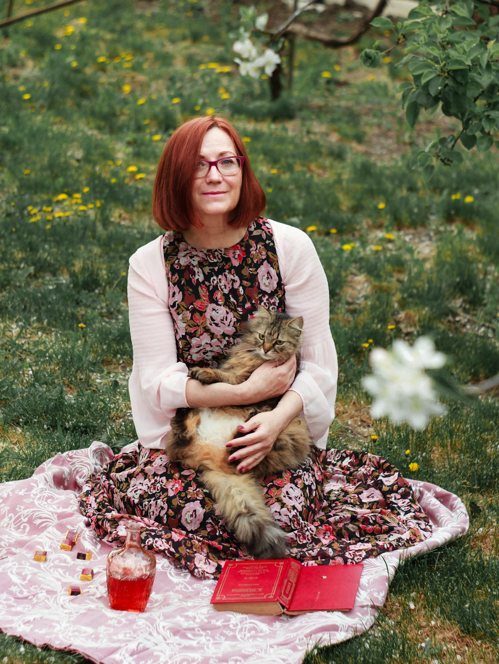 woman in white cardigan sitting on pink textile on green grass field during daytime