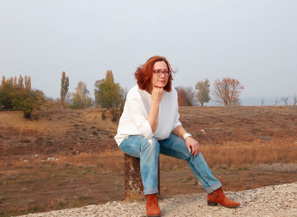 Mujer con camisa blanca de manga larga y jeans de mezclilla azul de pie en un campo marrón durante el día