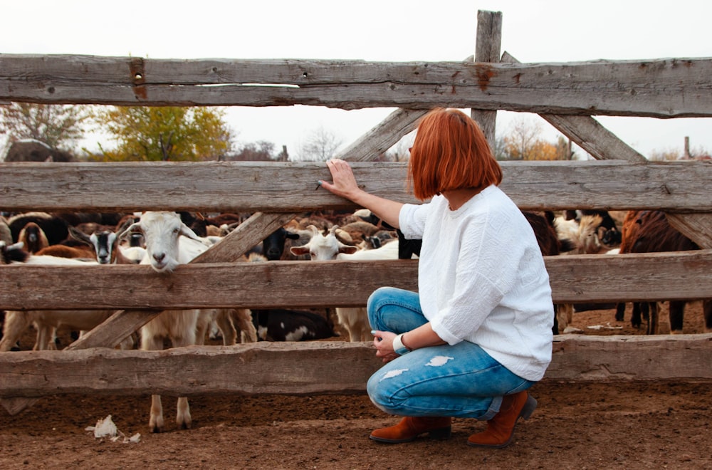 woman in white long sleeve shirt and blue denim jeans sitting on brown wooden fence