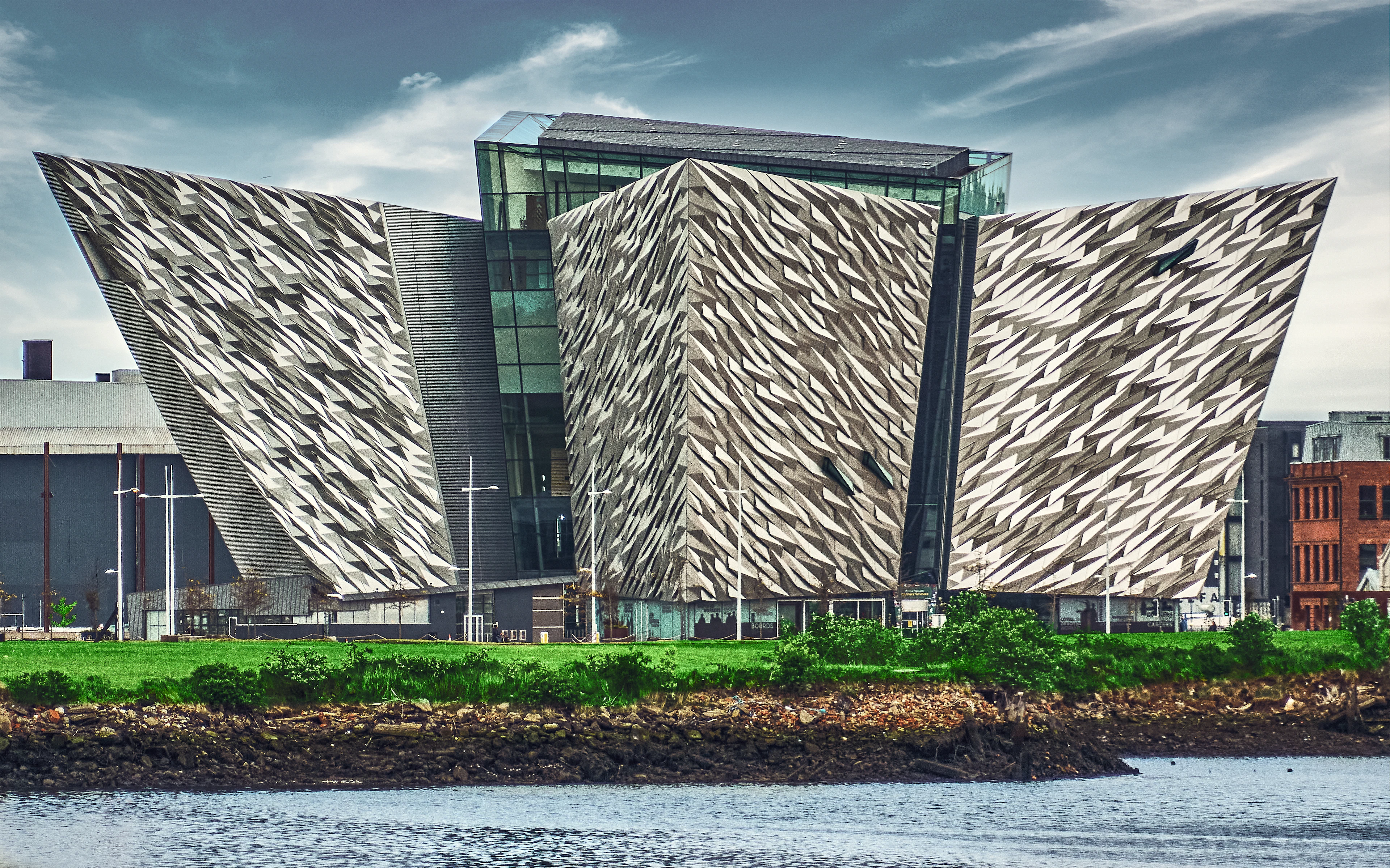 The angular silver hull-shaped facades of the Titanic Belfast museum seen from across the water.