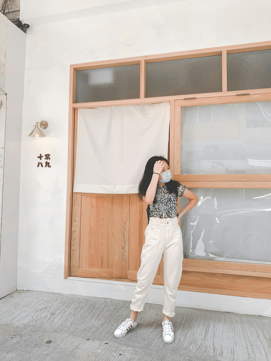 woman in black and white polka dot shirt and white pants standing beside brown wooden door