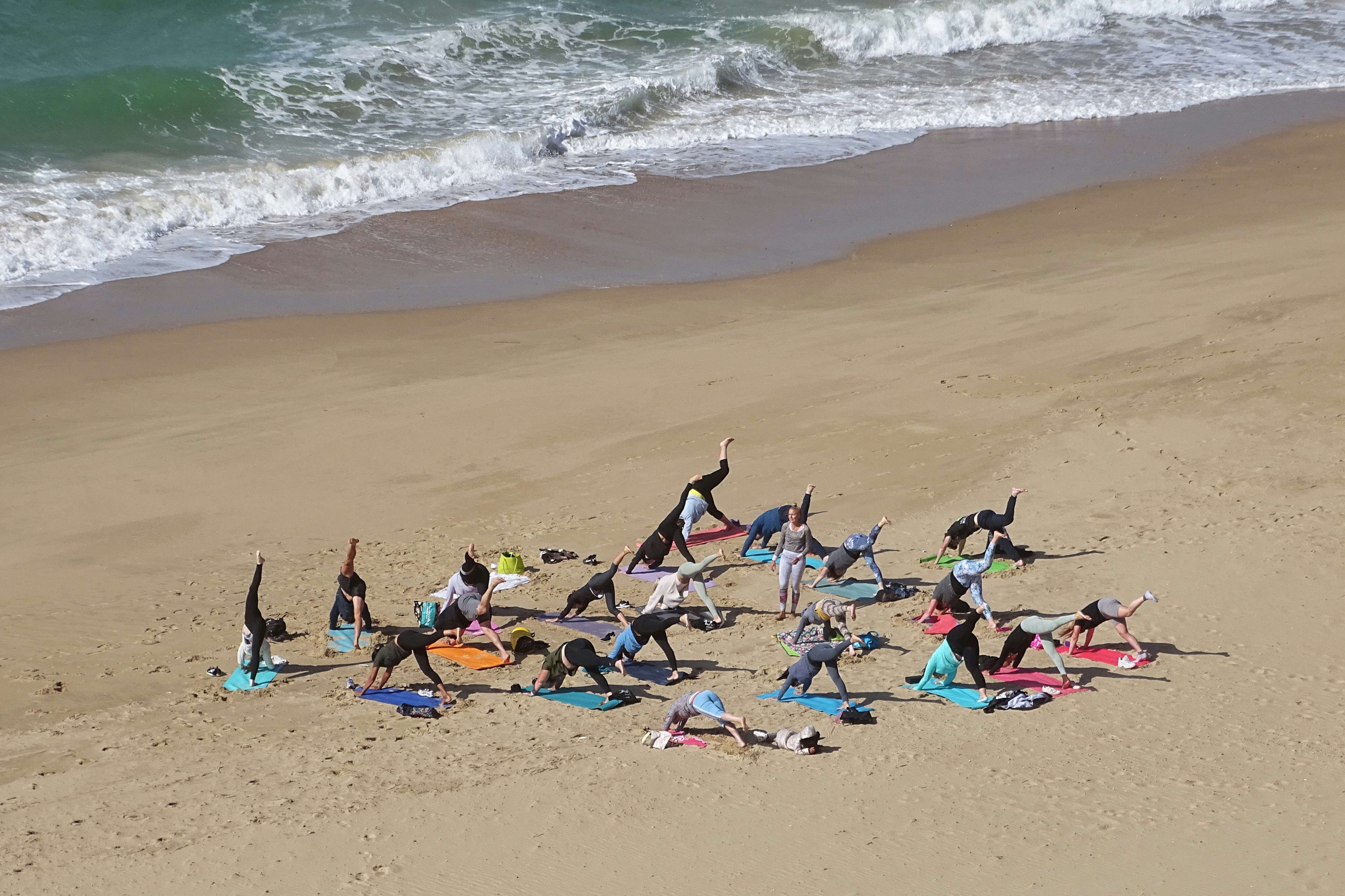 Group yoga session on sandy beach at sunrise with ocean in background