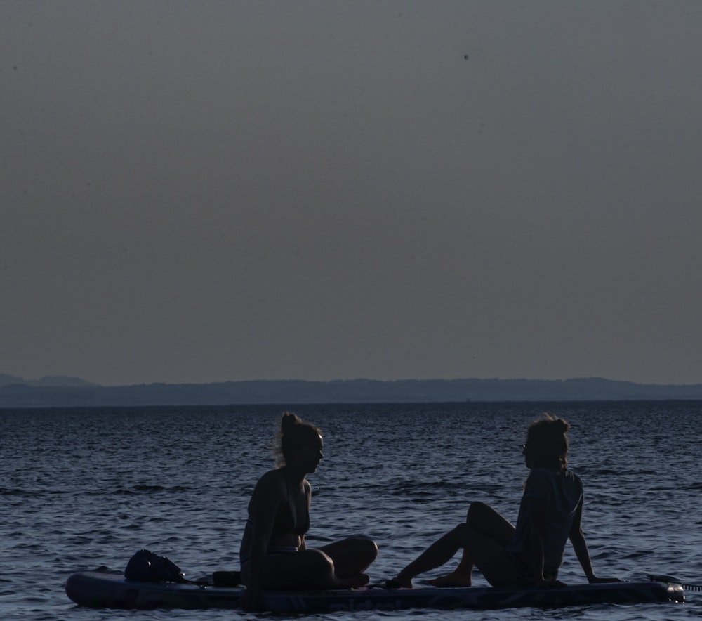 silhouette of people sitting on rock in the sea during daytime