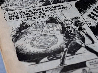 A comic book illustration featuring a confident announcer declaring Arnie Stodgman as the new heavyweight champion of the world. The image includes an oversized character with a large abdomen, surrounded by cheering figures. The style is classic black and white, with bold text and dynamic expressions.