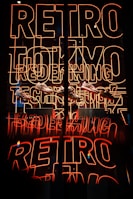 Bright neon sign featuring the words 'RETRO TOKYO TECH' in orange-red hues, with a reflection creating a mirrored effect. Below the neon, several sneakers are displayed.