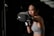 A woman in athletic wear is intensely focused as she throws a punch, wearing boxing gloves. Her stance and expression suggest concentration and determination. The background is dark, emphasizing her figure and action.