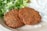 Two crispy falafel patties are placed on a beige plate, accompanied by a side of chopped leafy greens and a dollop of creamy white sauce.