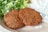Two crispy falafel patties are placed on a beige plate, accompanied by a side of chopped leafy greens and a dollop of creamy white sauce.