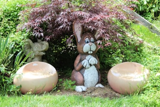 A whimsical outdoor statue of a rabbit nestled among garden plants.