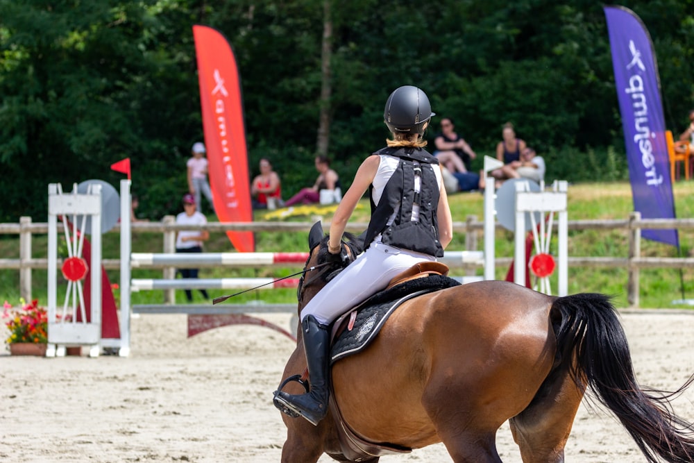 Mann in schwarz-weißem Helm reitet tagsüber auf braunem Pferd