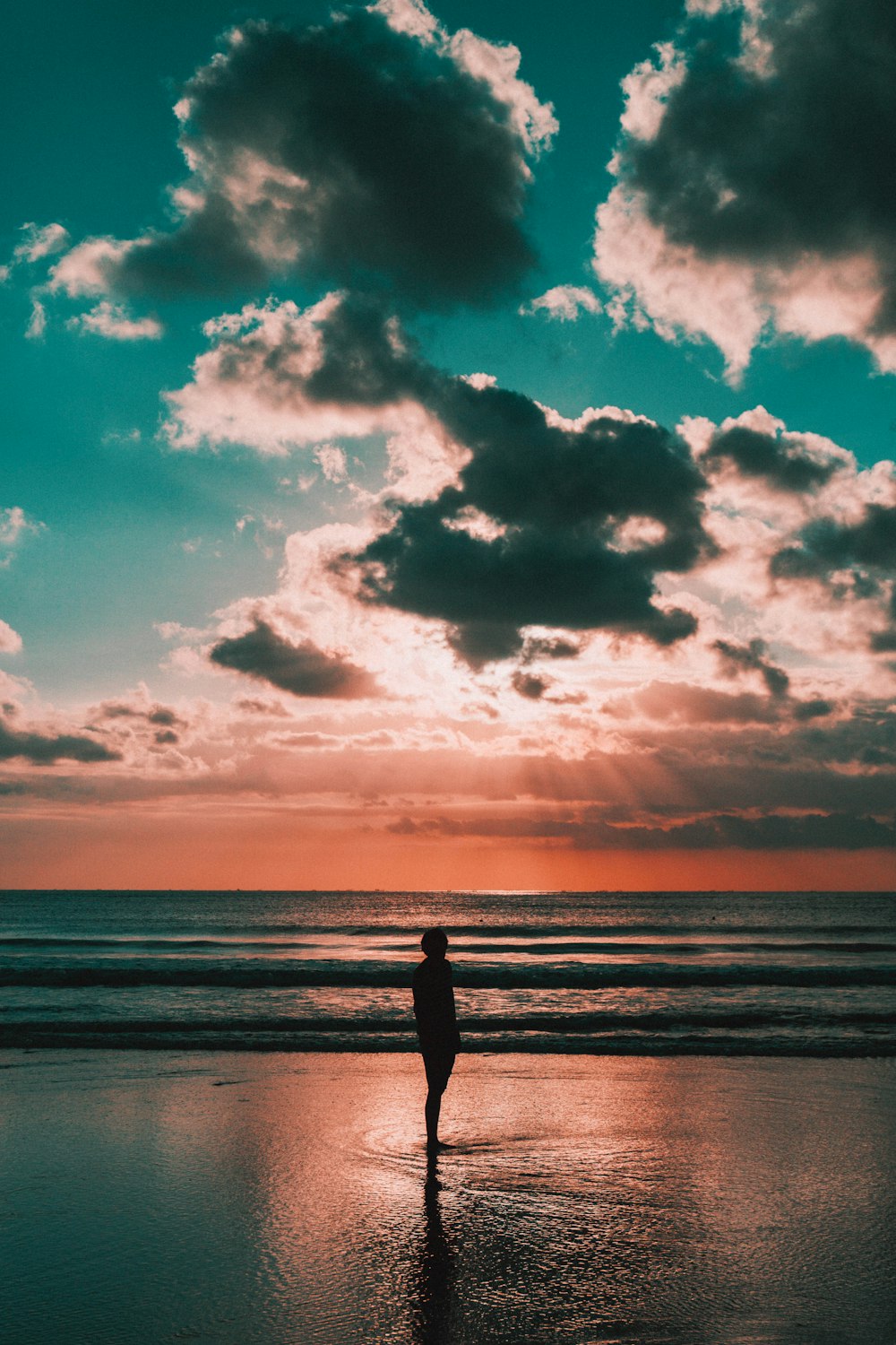 silhouette de personne debout sur la plage pendant le coucher du soleil