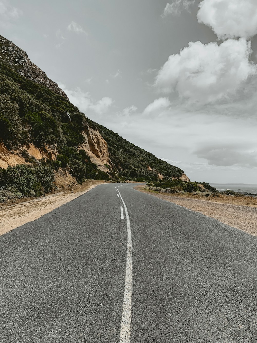 gray asphalt road near brown mountain under white clouds during daytime