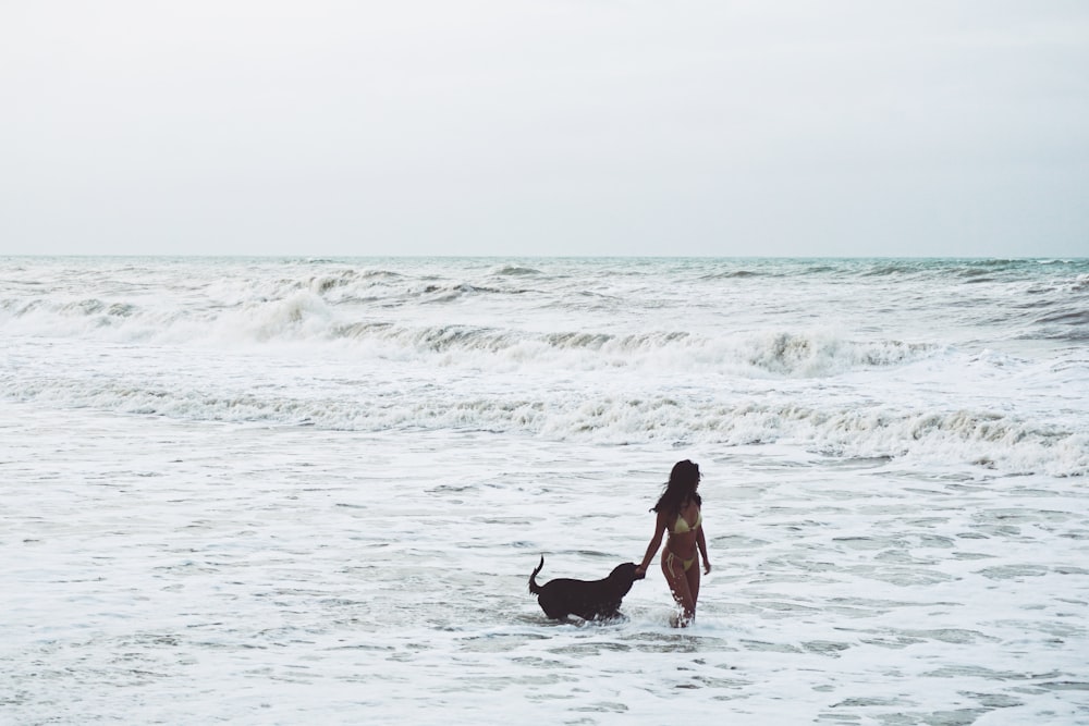 Mujer en vestido negro sosteniendo labrador retriever negro en la playa durante el día