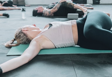 woman in white sports bra and black shorts lying on green yoga mat