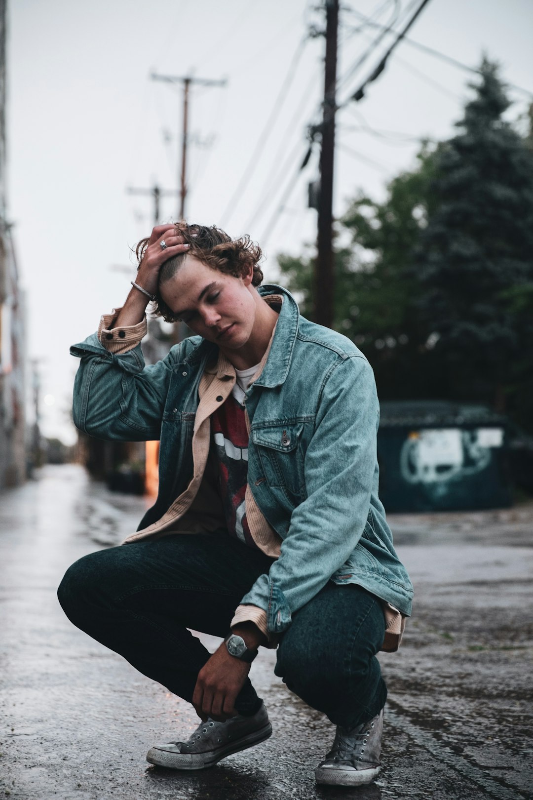 woman in green denim jacket sitting on gray concrete pavement during daytime