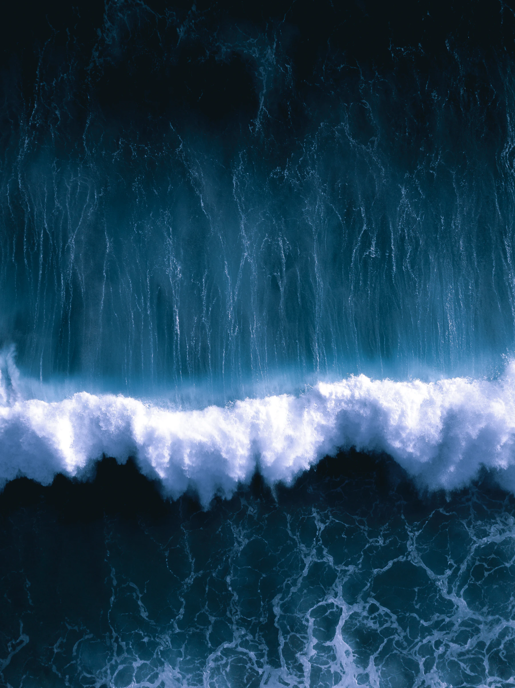 An aerial view of a powerful ocean wave moving across calm deep water