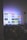 A flat-screen television is displaying a variety of streaming app icons, including Netflix, Prime Video, Spotify, and ITV Hub among others. The TV is placed on a media console with a small potted plant beside it. A tall lamp stands to the right, and a faint, ambient light casts a purple hue on the wall above the TV.