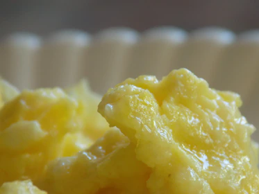 Close-up of hands holding fresh pasture butter next to rustic scrambled eggs.