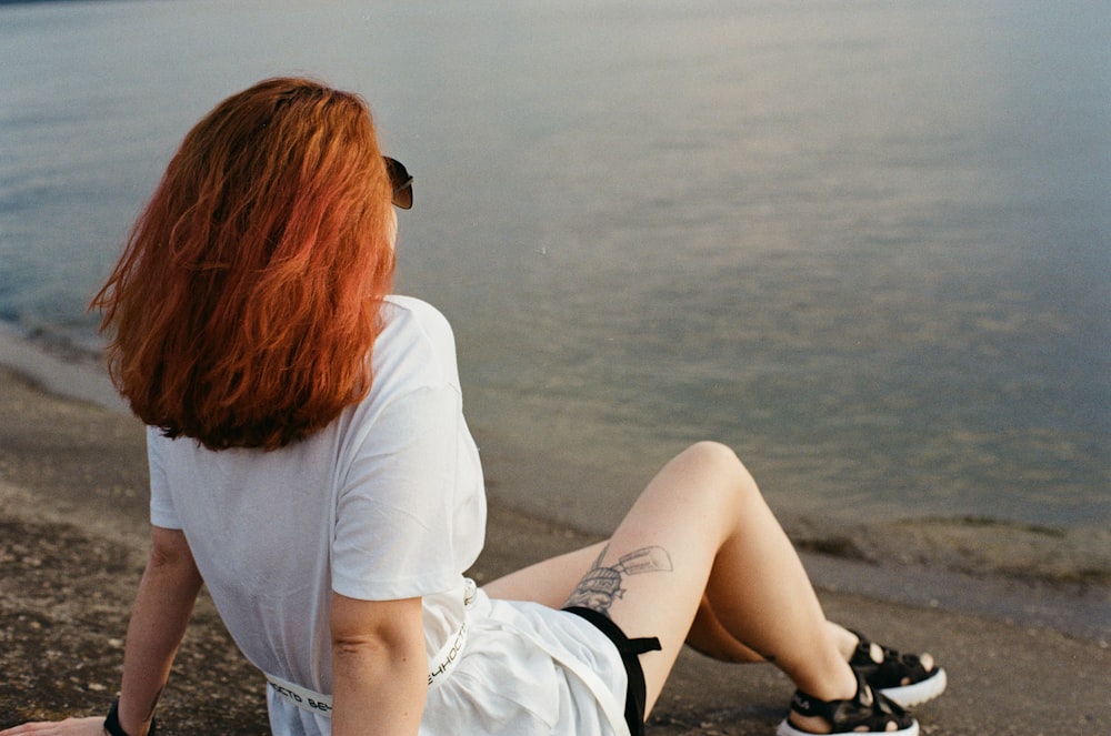 woman in white shirt and black shorts sitting on gray concrete floor