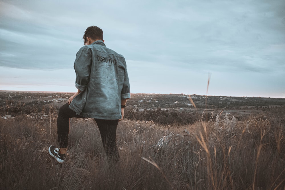 man in blue denim jacket standing on brown grass field during daytime