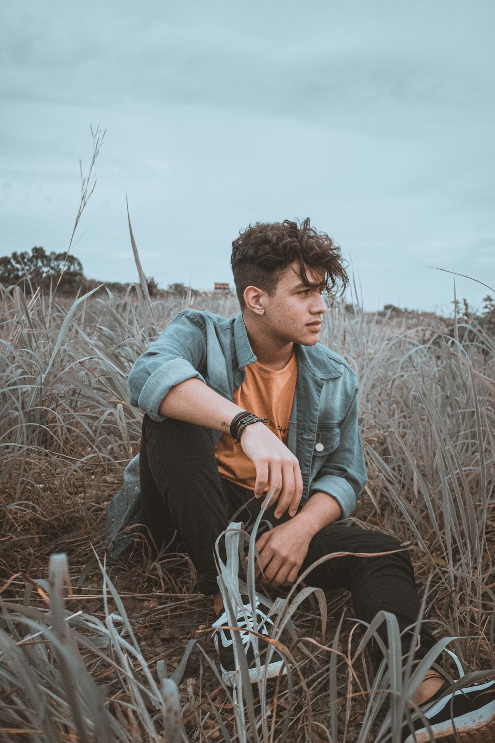 man in blue denim jacket sitting on grass field during daytime