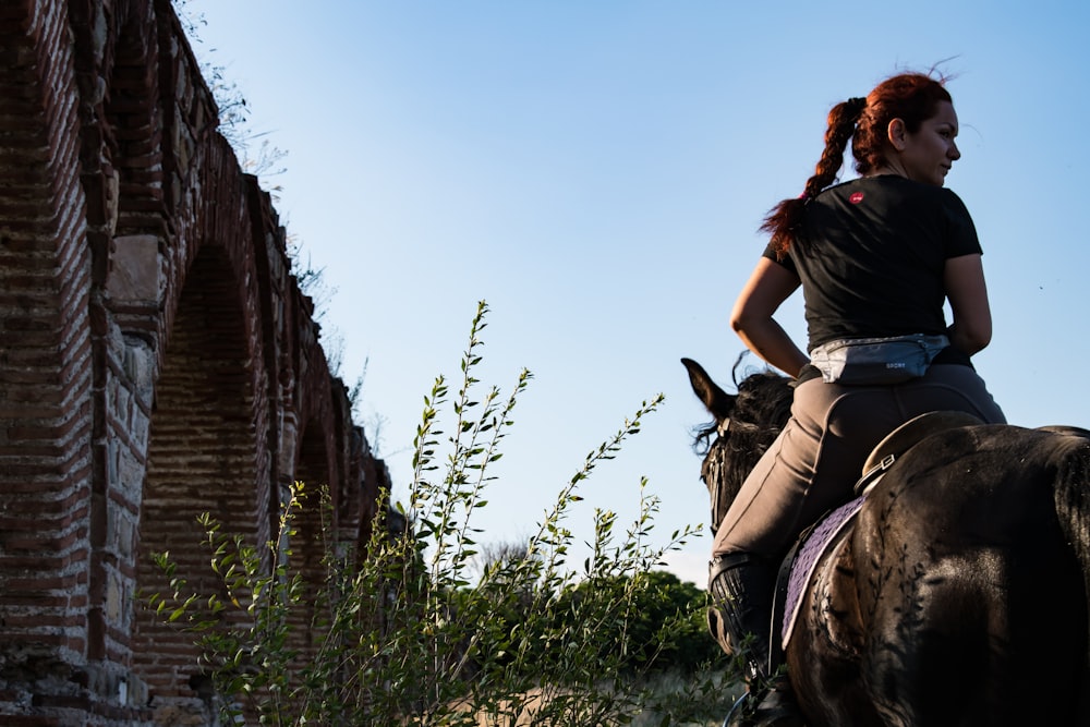 woman in black t-shirt and brown pants riding on brown horse during daytime