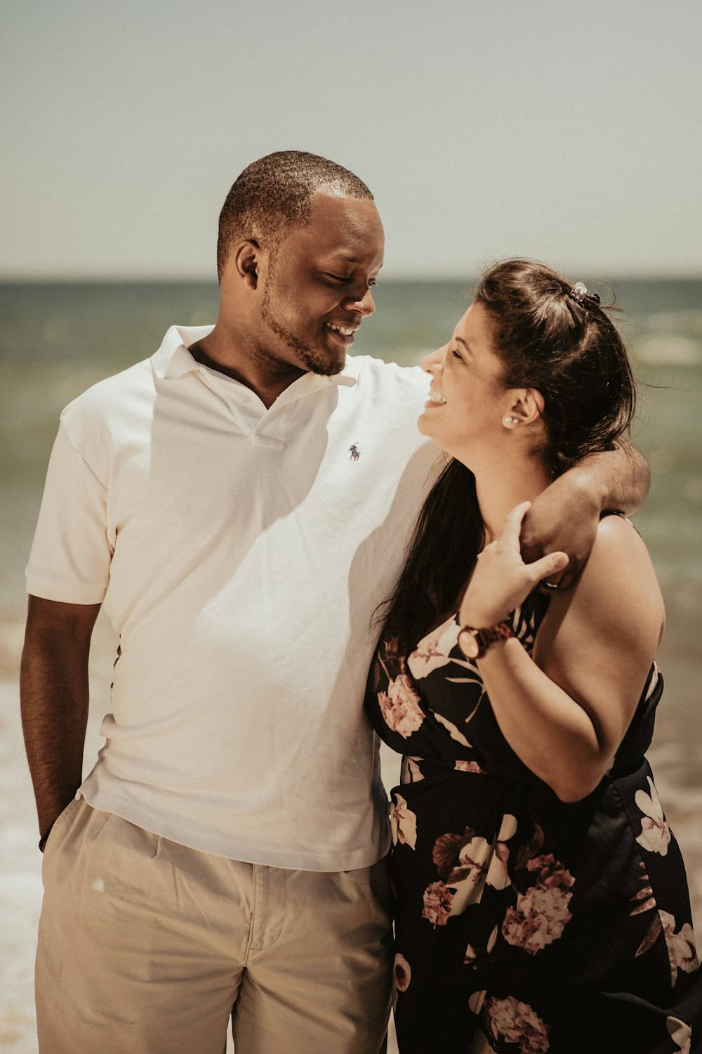 homem na camisa polo branca beijando a mulher no vestido floral preto e cor-de-rosa