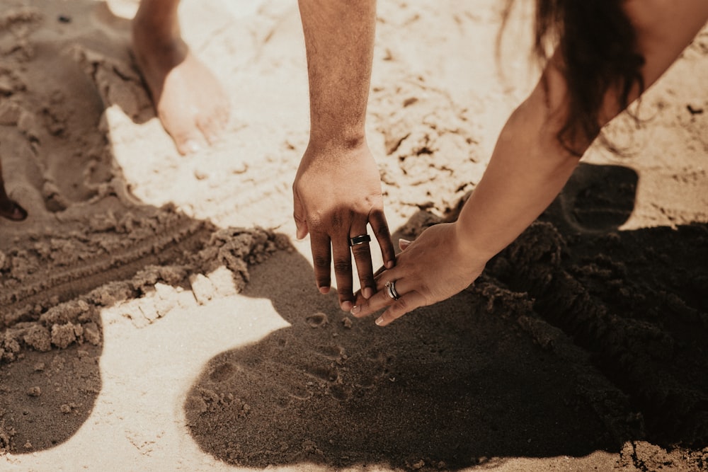 person holding hands of woman on sand