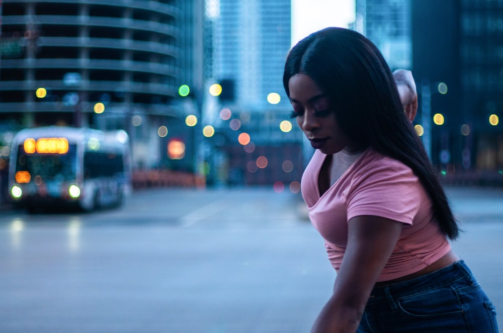 woman in pink shirt and blue denim jeans standing on road during night time