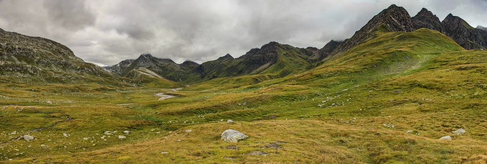 green grass field near mountain under white clouds during daytime