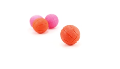 Several small basketball toys are placed on a plain white background. The balls are textured and vary in color, with two being orange and two pink. The focus is on the basketball in the foreground, which is distinctly highlighted.