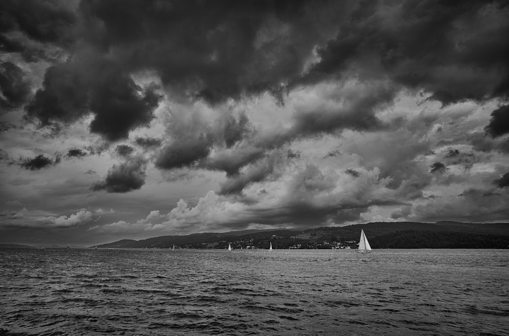 grayscale photo of sailboat on sea under cloudy sky