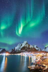 Green aurora borealis above the snowy mountains and coastal village of Reine, Lofoten