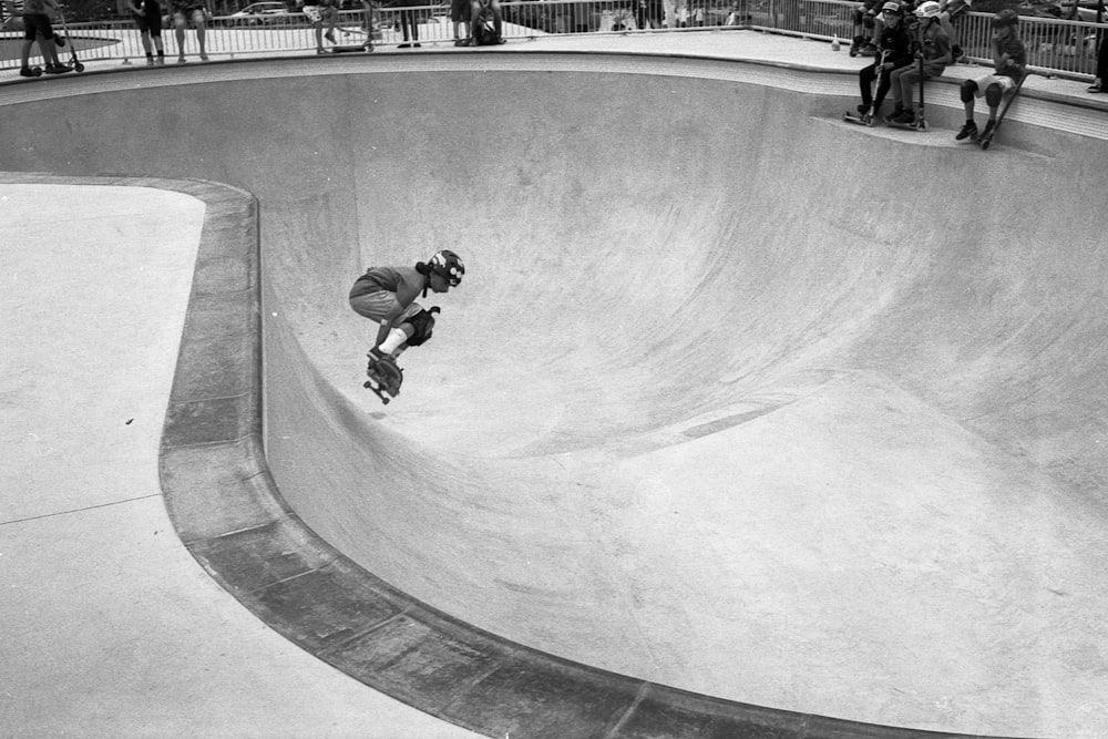 foto em tons de cinza do homem em jaqueta preta e calças andando de skate