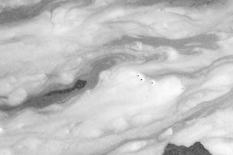 Swirling patterns of foam on the surface of liquid with a few small bubbles dispersed throughout. The textures are varied, giving a flowing appearance to the foam.