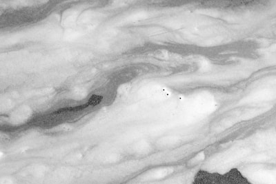 Swirling patterns of foam on the surface of liquid with a few small bubbles dispersed throughout. The textures are varied, giving a flowing appearance to the foam.