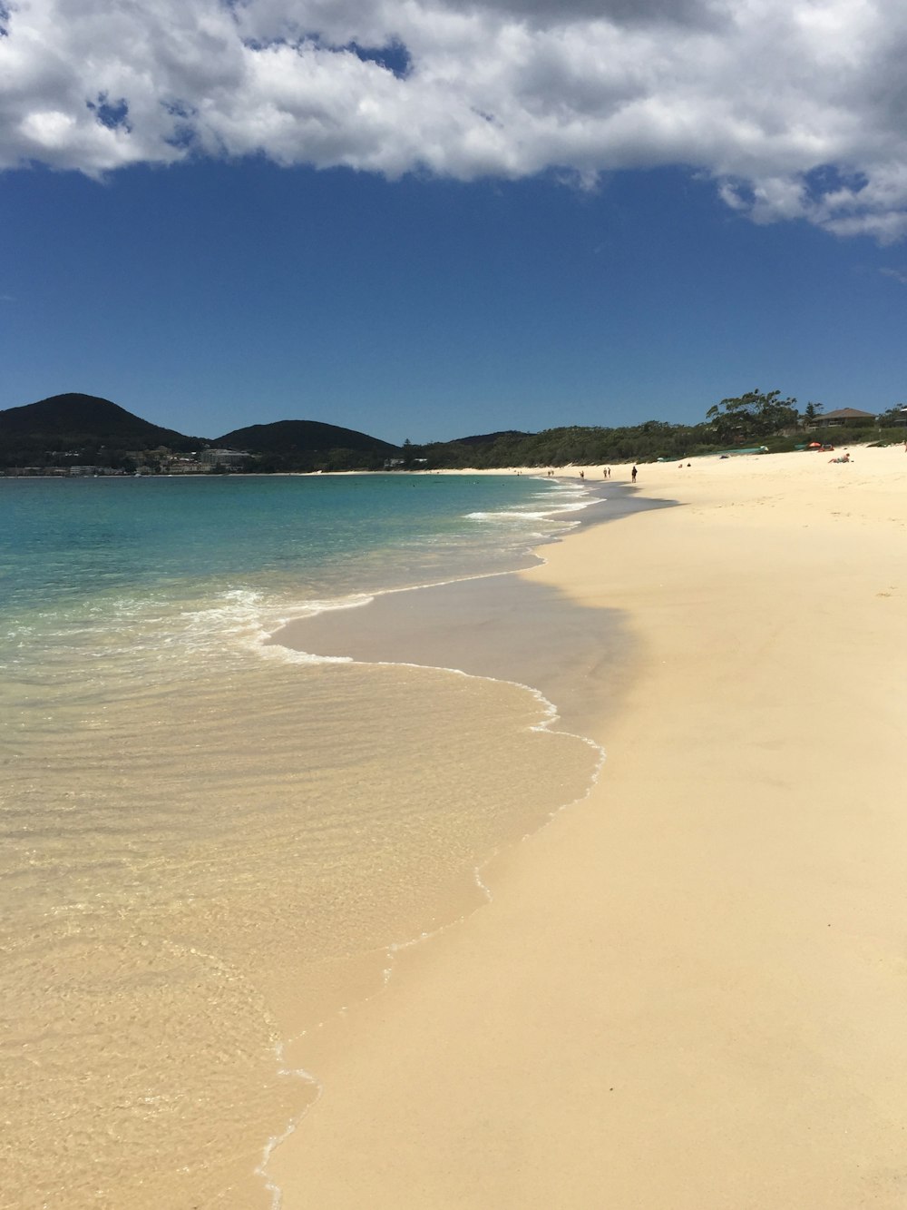 brown sand beach with green mountain in distance under blue sky during daytime