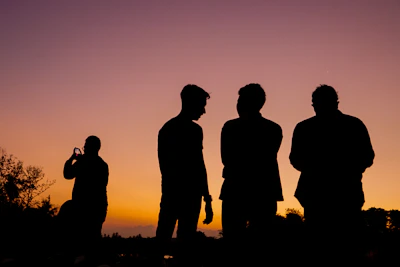 silhouette of 3 men standing on grass field during sunset