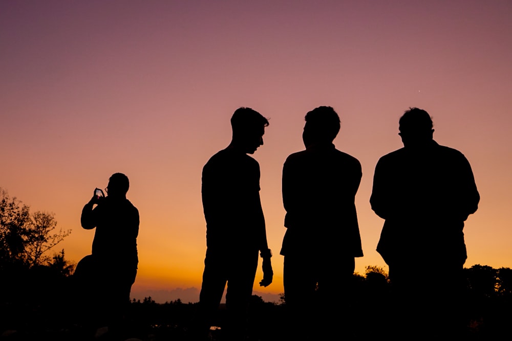 silhouette of 3 men standing on grass field during sunset