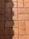 A section of red-orange floor tiles, each tile rectangular in shape, arranged in a regular pattern with visible grout lines in between. The tiles exhibit some signs of wear and darker patches, suggesting age or frequent use. A shadow is cast across part of the tiles, adding contrast to the composition.