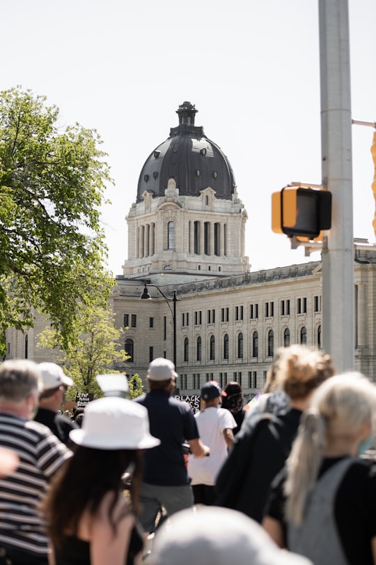 people walking near gray concrete building during daytime in Saskatchewan Legislative Building Canada