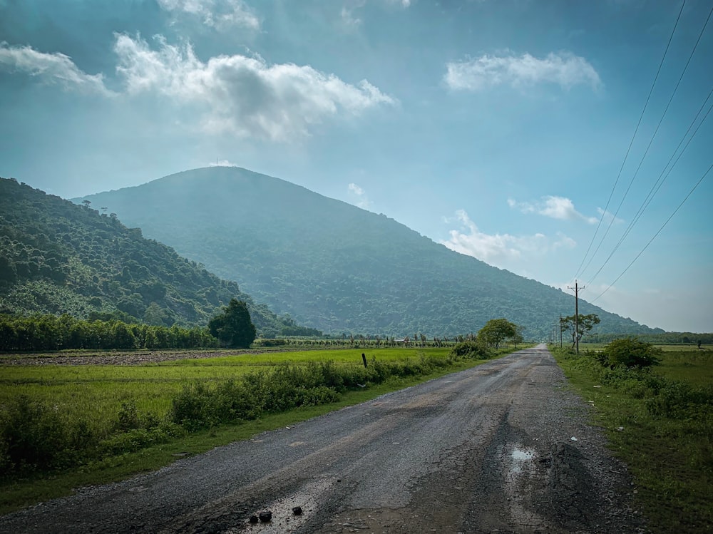 green grass field near mountain under white clouds and blue sky during daytime